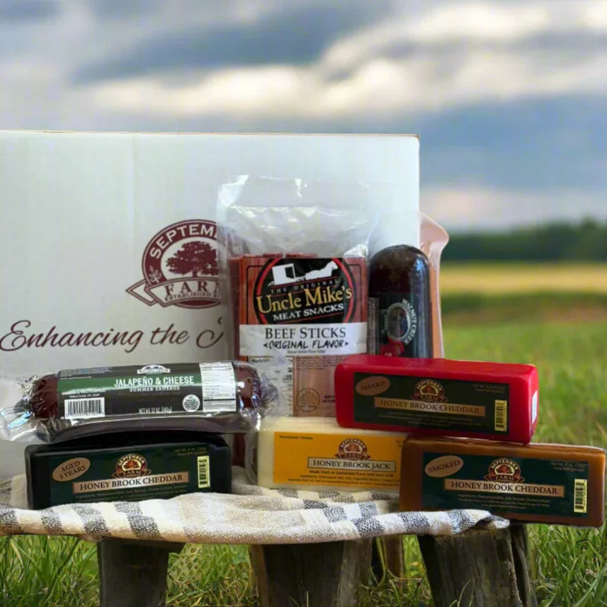 Assorted meats and cheeses on a wooden stool with a 'September Farm' branded box in a field.
