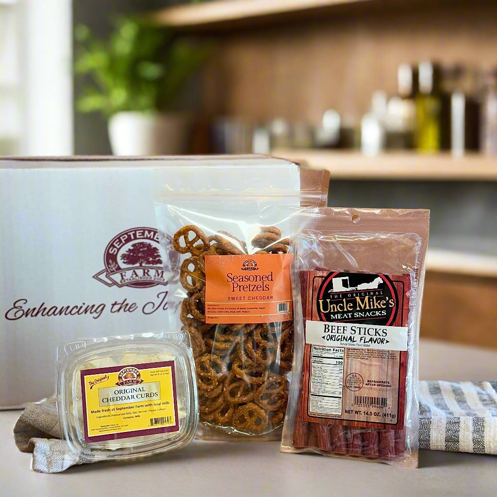Assorted snack packages including beef sticks, pretzels, and cheddar crisps on a wooden surface.